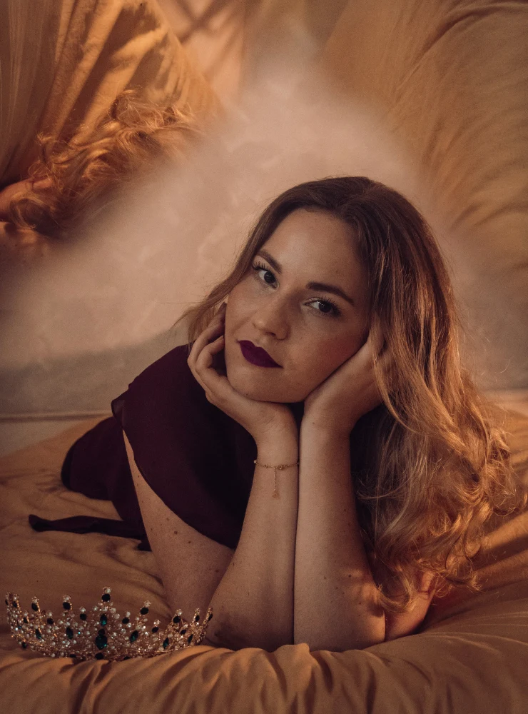 Corinna Kehl liegt auf goldenem Satin, das Kinn in die Hände gestützt, vor ihr eine Krone